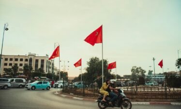 A man riding a motorcycle down a street next to red flags